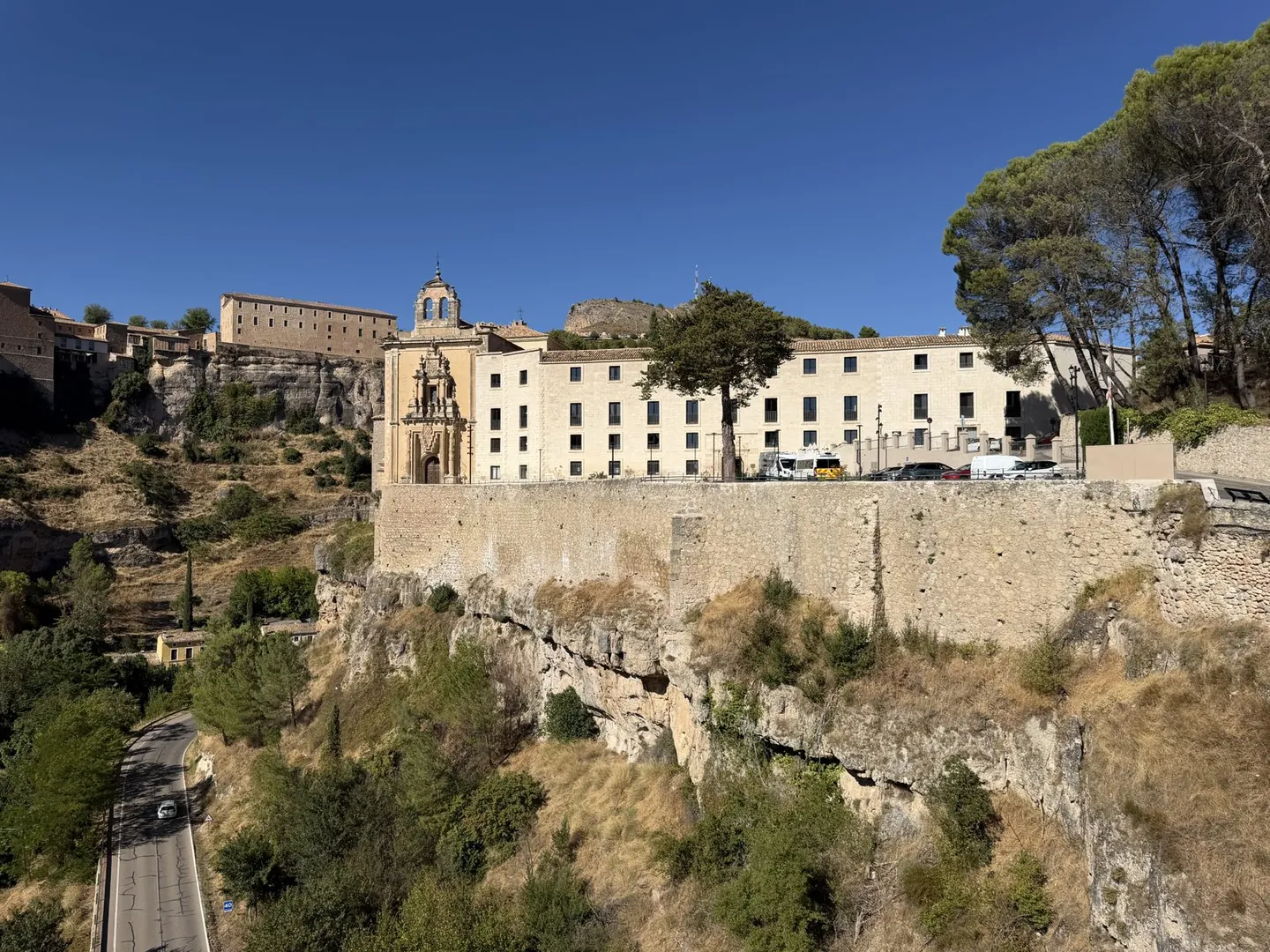 Historic Spanish buildings perched on top of a limestone cliff above a winding road