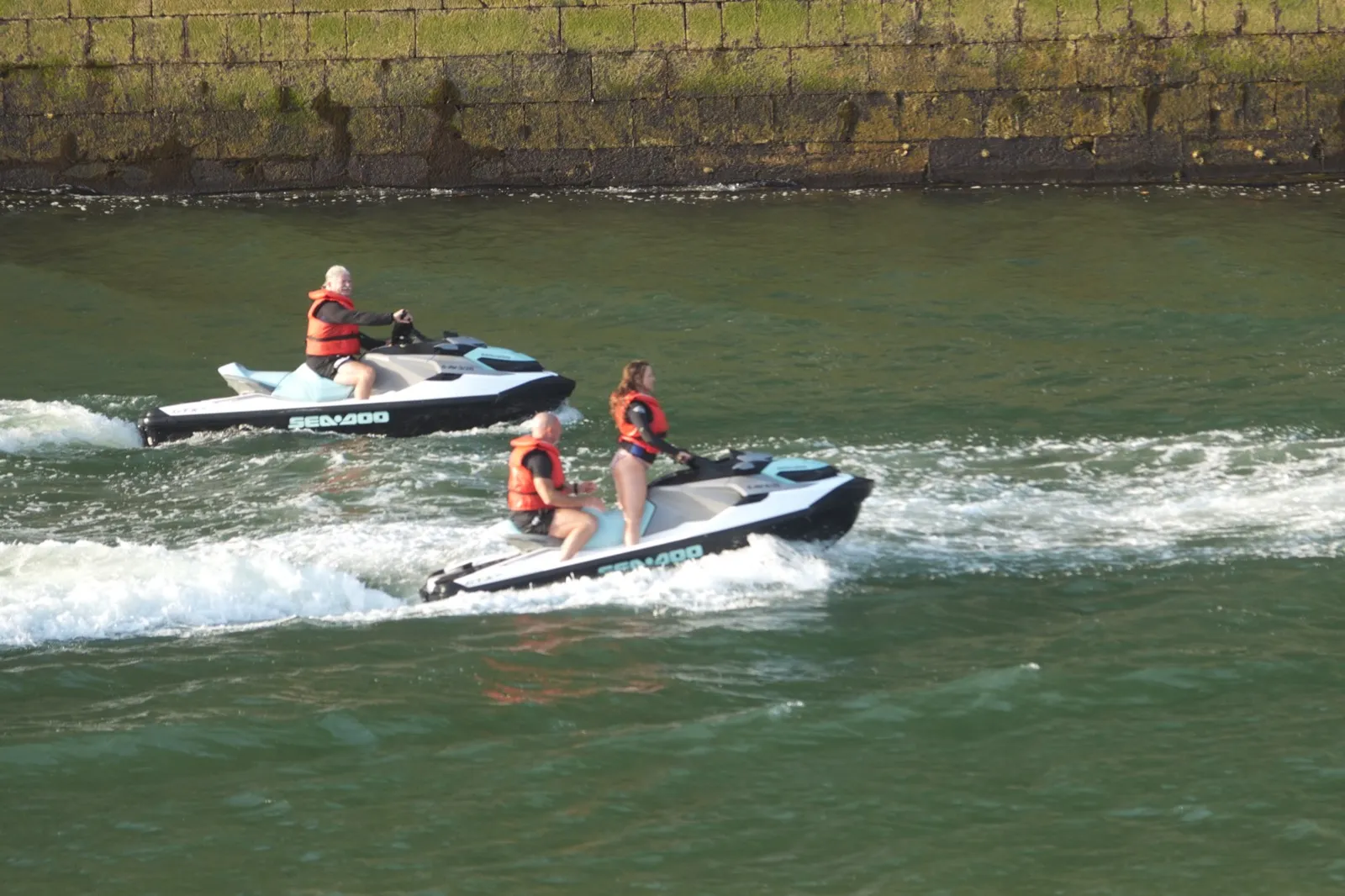 Two jet skis carrying Cannonball riders along the harbour wall in Ribadesella