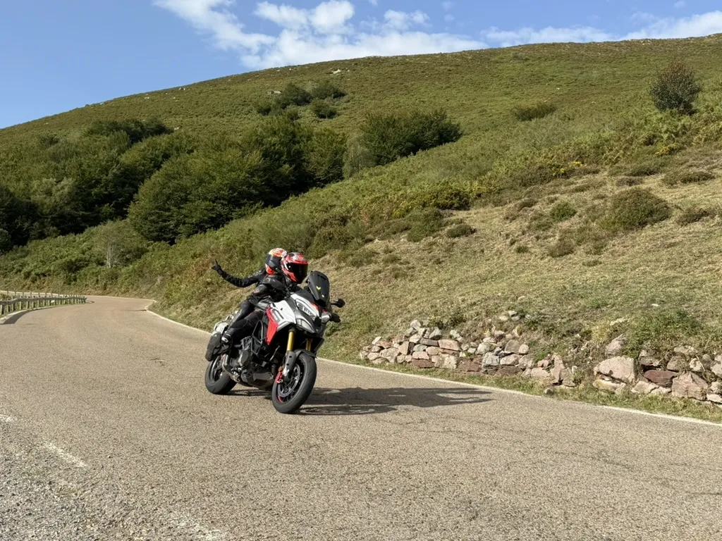 Lars and Ina riding a touring motorcycle through a sweeping mountain bend in northern Spain