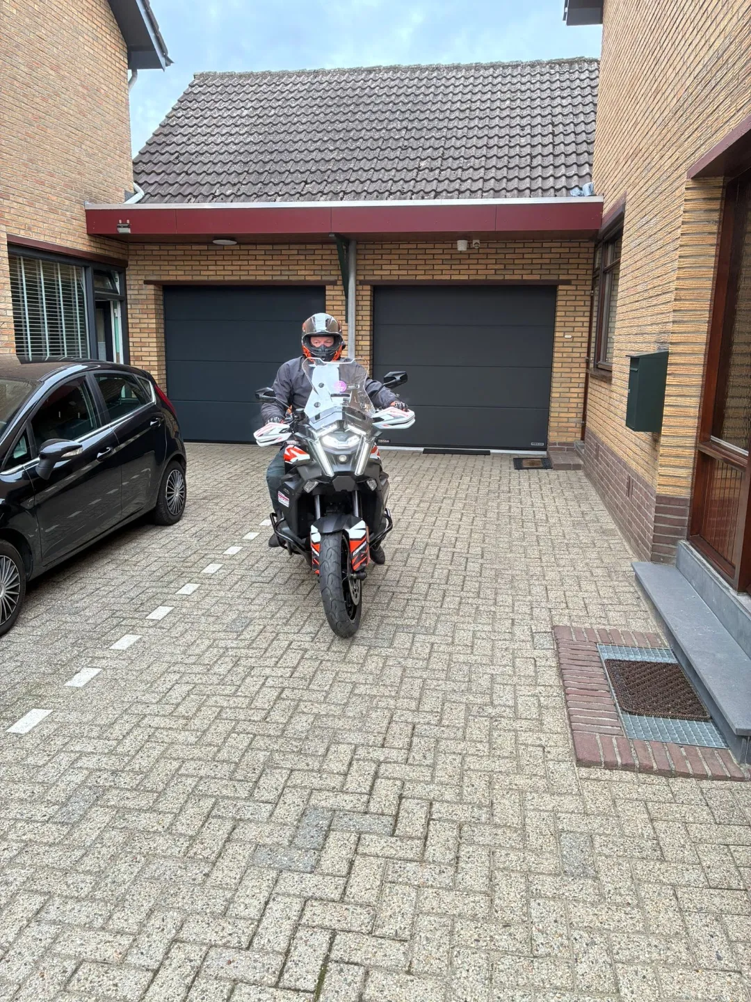 Rider on an orange and white adventure motorcycle leaving a driveway in Limburg, the Netherlands