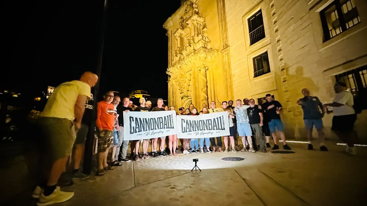 Cannonball riders gathered with banners outside a floodlit historic building at night