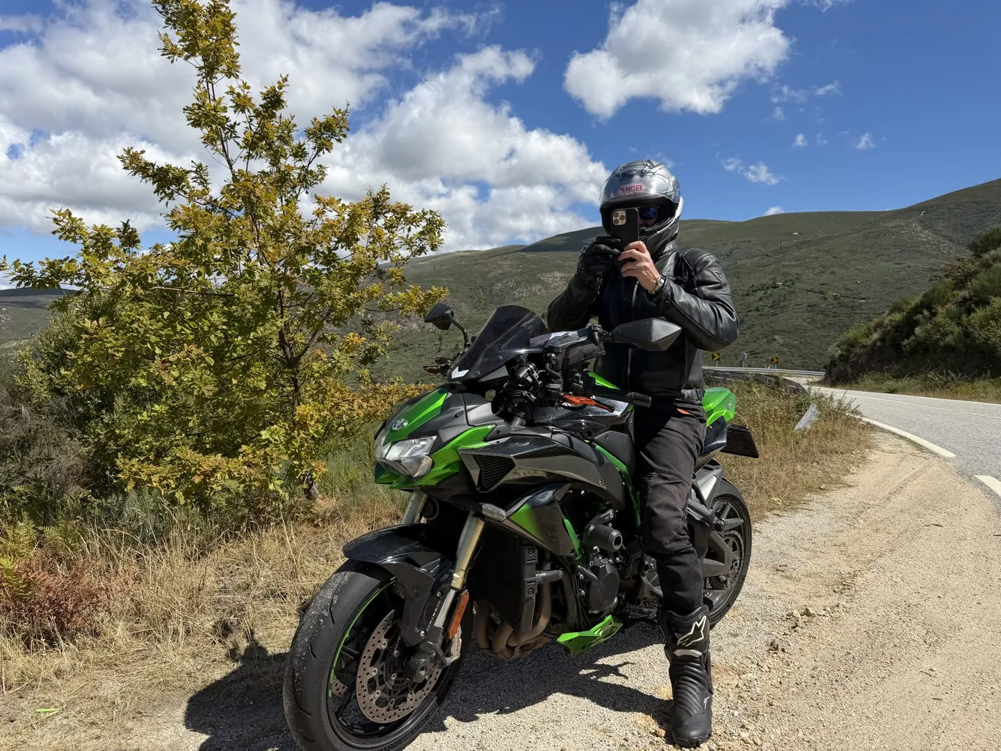 Rider on a green Kawasaki naked bike stopped beside a sweeping mountain road in Portugal