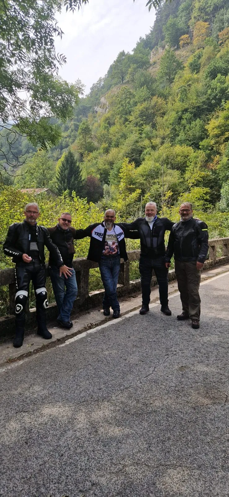 Five riders in leathers posing on a bridge on a wooded mountain road on the way to the start