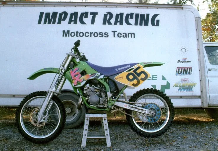 Green Kawasaki motocross bike number 95 in front of the Impact Racing motocross team van