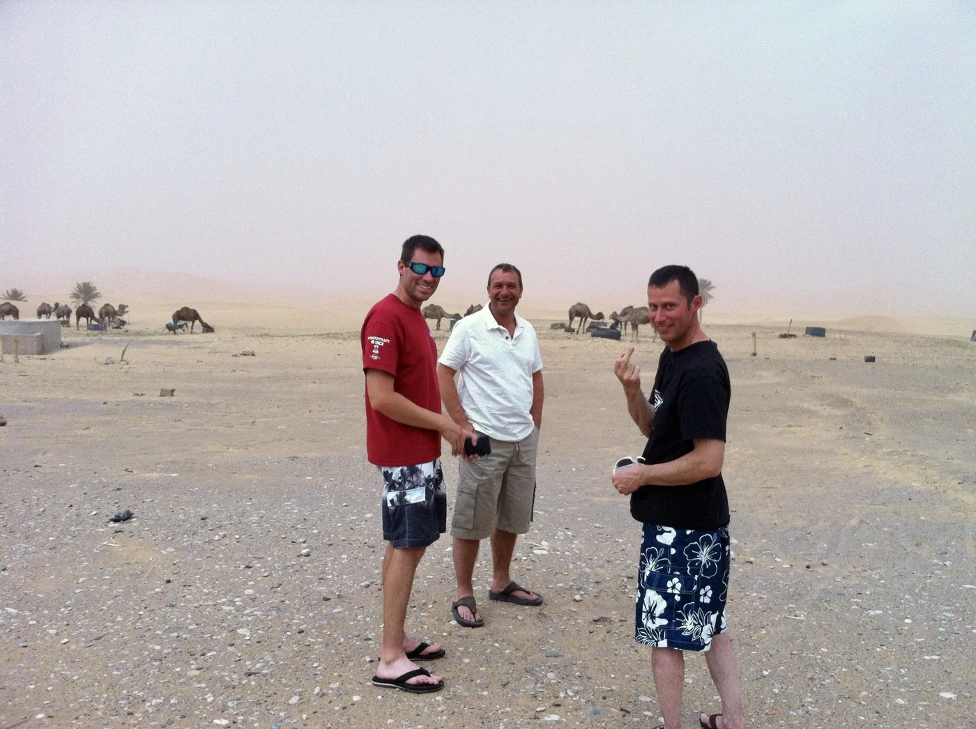 Jeremy Simmons with two friends in the Moroccan desert with camels behind them