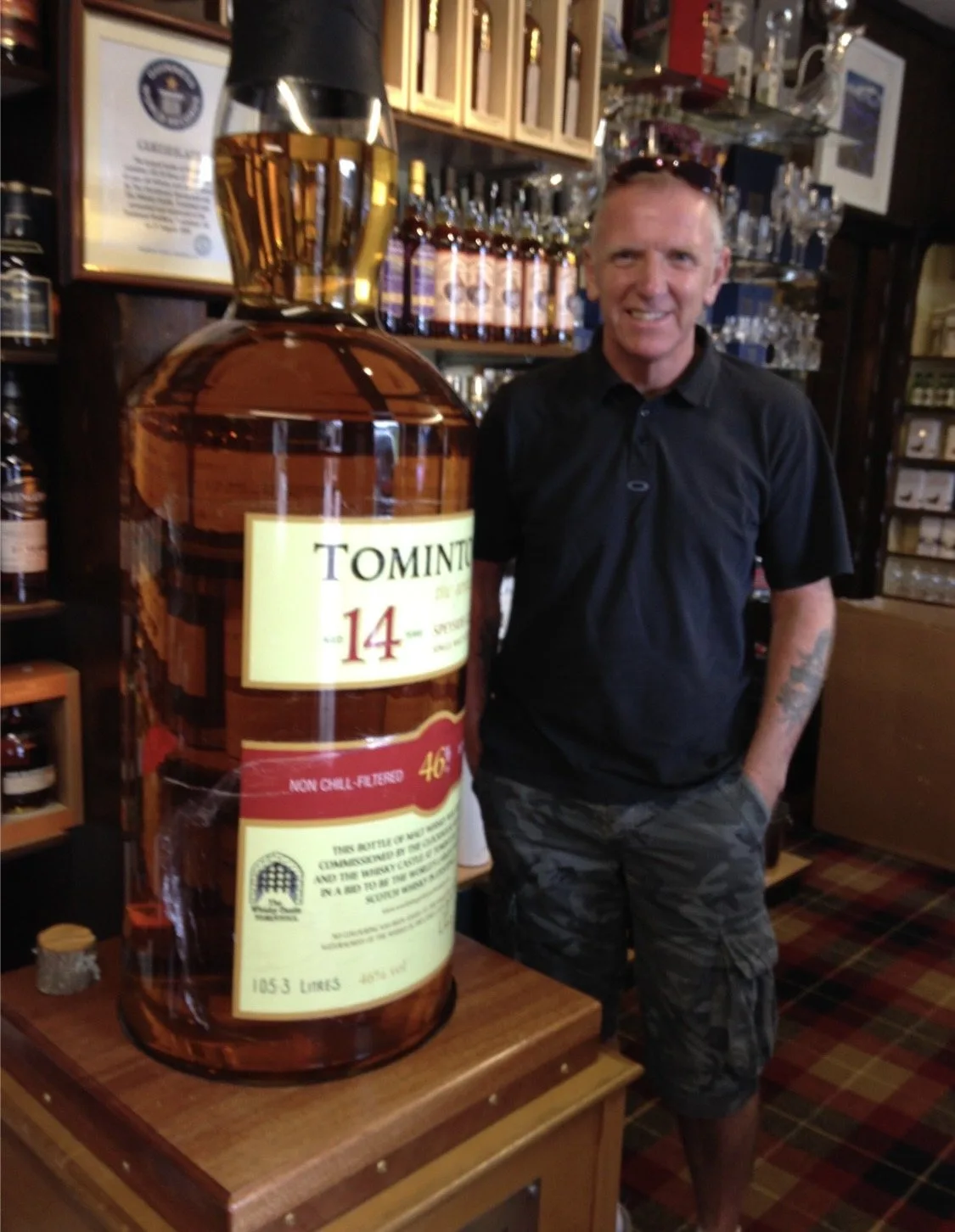 Jim Horne beside a giant Tomintoul 14 year old whisky bottle in the Tomintoul whisky shop, Tomintoul