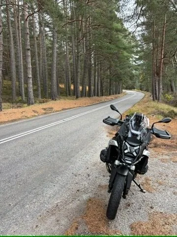 Motorcycle parked beside a pine forest road in the Cairngorms