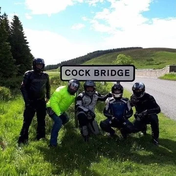 A group of motorcyclists by the Cock Bridge sign at the foot of the Lecht, Alan Jones in a yellow waterproof jacket