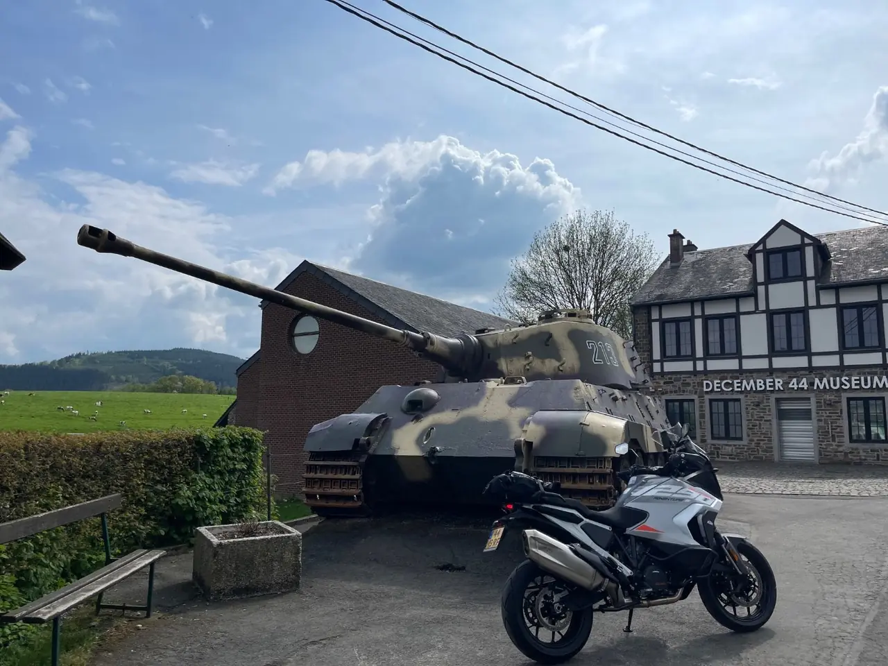KTM 1290 Super Adventure parked in front of the Tiger II 213 tank monument at La Gleize, with the December 44 Museum behind