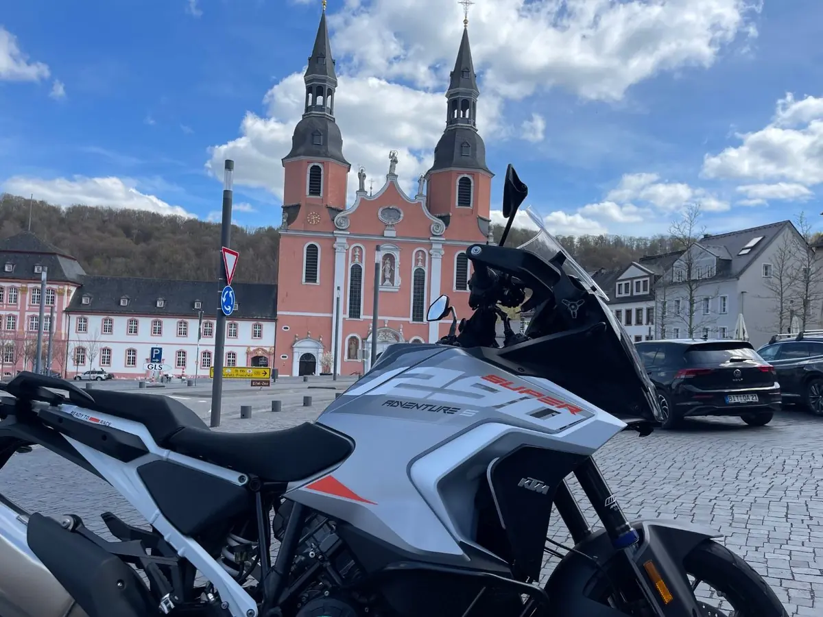 A KTM 1290 Super Adventure S parked on the square at Prüm in front of the twin-towered pink Salvatorbasilika
