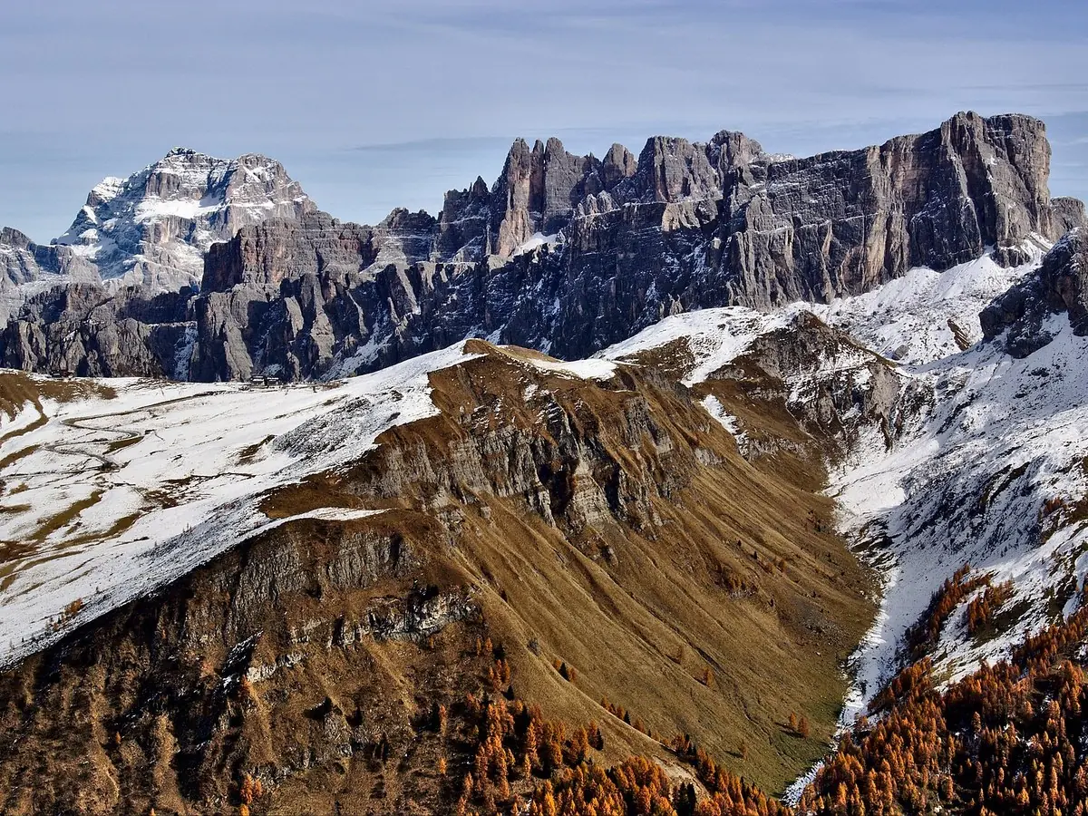 The snow-dusted rock towers and long scree ridges of the Nuvolau group seen from the Passo Giau, with golden autumn larch below