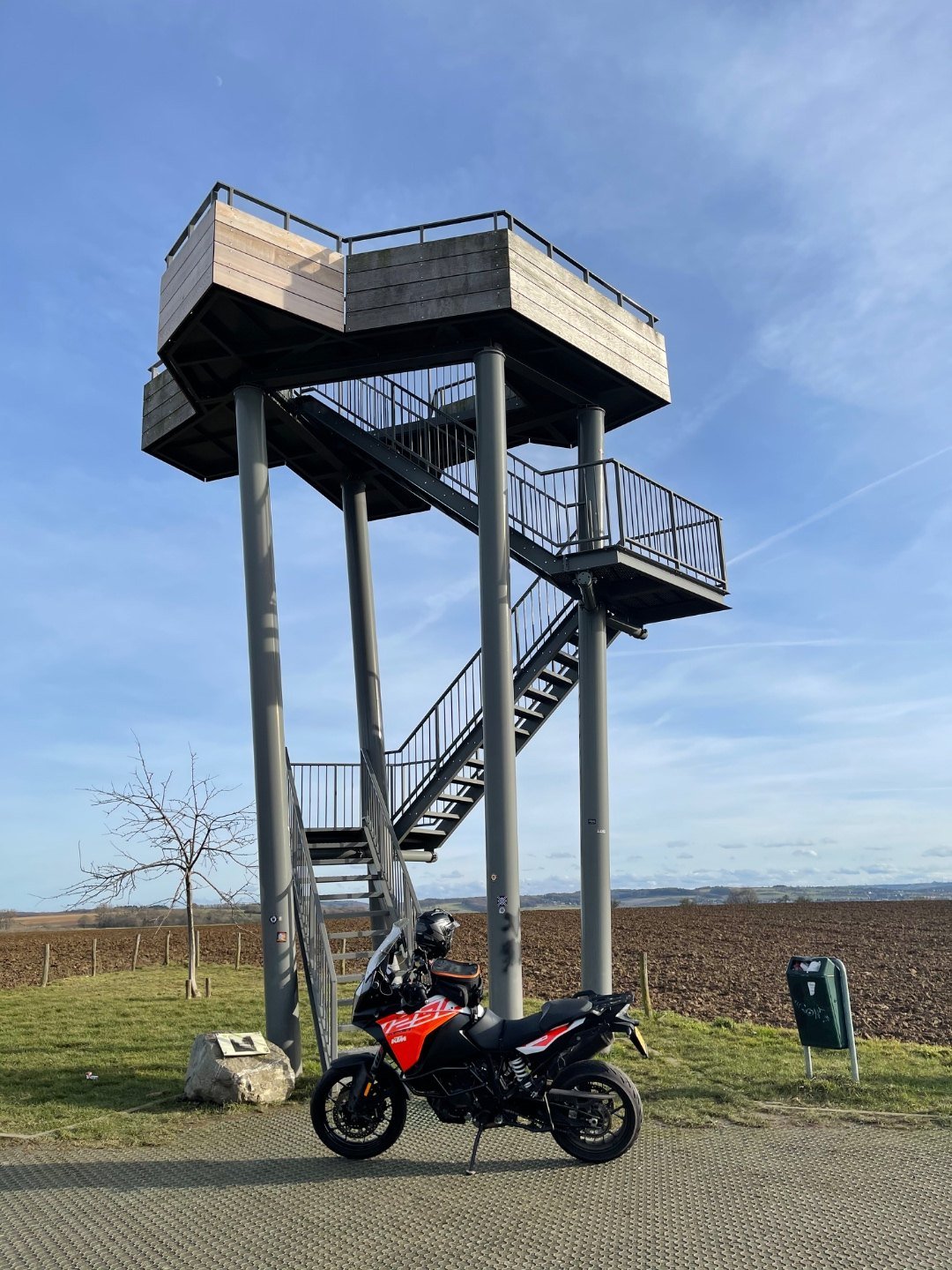 A KTM 1290 Super Adventure S parked beneath the steel and timber lookout tower on the Mescherheide