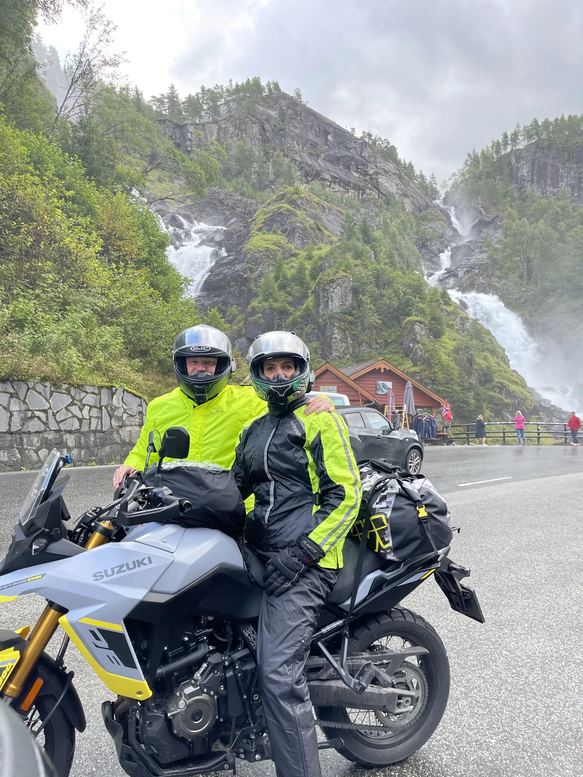 Alan and Belinda in fluorescent rain jackets on a Suzuki in front of a tall waterfall in Norway